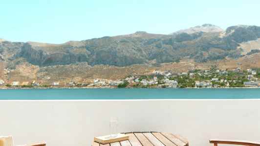 To stoler og et bord på en balkong med utsikt over en innsjø og fjell. (AI-generert tekst)