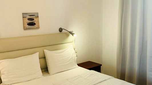 En oppredd seng med hvitt sengetøy og to brettede håndklær. Veggdekorasjon og gardiner i bakgrunnen. (AI-generert tekst)