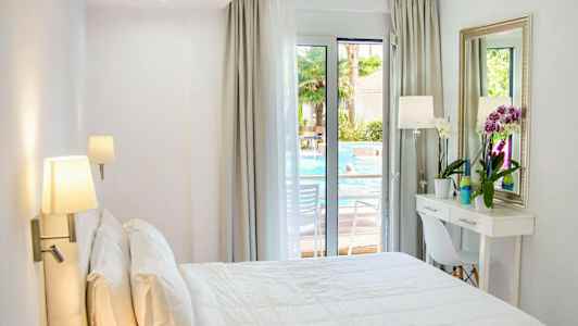 Lyst hotellrom med en oppredd dobbeltseng, et skrivebord og vindu mot bassengområdet. (AI-generert tekst)