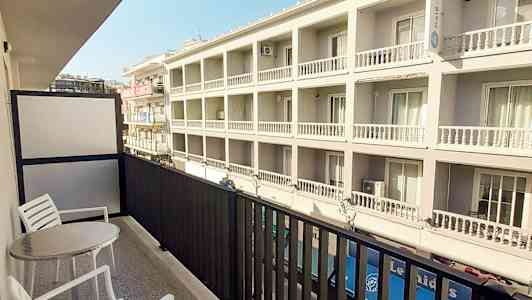 En balkong med to stoler og et bord, utsikt over en moderne bygning. (AI-generert tekst)