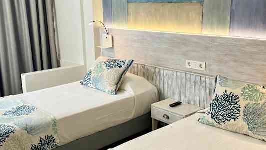 To enkeltsenger med blått og hvitt korallmønster på sengetøyet i et hotellrom. (AI-generert tekst)