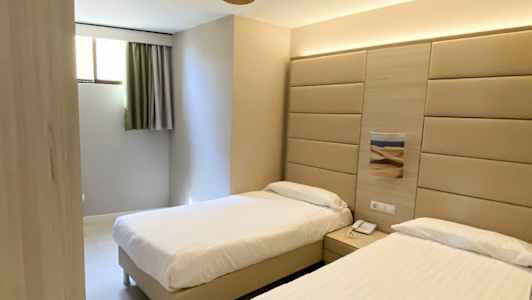 Et hotellrom med to enkeltsenger, veggpanel bak sengene og en takvifte. (AI-generert tekst)