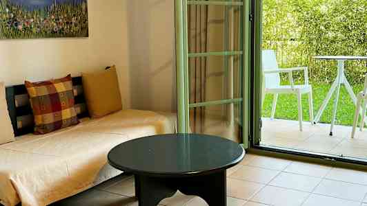 Rom med sofaer, et bord og en åpen dør mot en frodig uteplass. (AI-generert tekst)