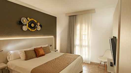 Et hotellrom med en dobbeltseng, dekorativ veggkunst over sengegavlen og et vindu med lyse gardiner. (AI-generert tekst)