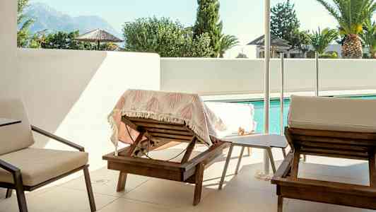 Bilde av en terrasse med solsenger, parasoll og basseng i bakgrunnen. (AI-generert tekst)