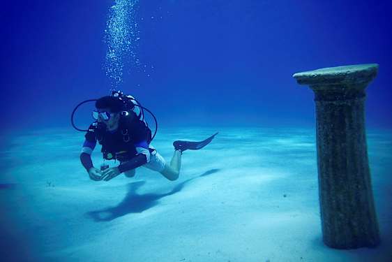 En dykker under vann nær en antikk søyle på havbunnen. (AI-generert tekst)