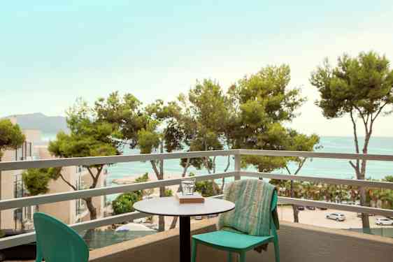 Utsikt fra en balkong med et bord og stol, utover trær og hav. (AI-generert tekst)