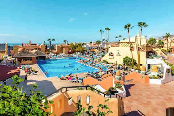 Et hotellområde med et stort basseng omgitt av solsenger og bygninger. (AI-generert tekst)