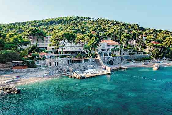 En bygning omgitt av grøntområder nær en strand med klart vann. (AI-generert tekst)