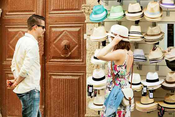 En person prøver en hatt ved et salgsbord med ulike hatter. (AI-generert tekst)