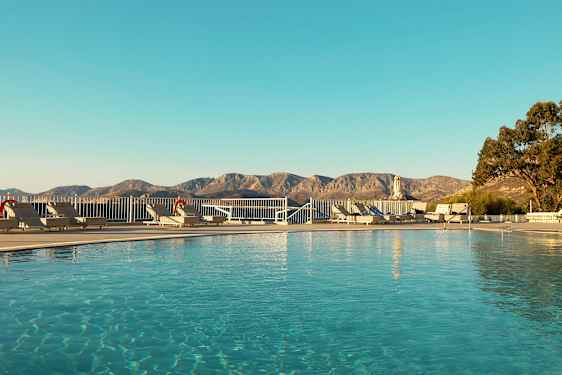 Bilde av et basseng omgitt av solsenger og med et fjellandskap i bakgrunnen. (AI-generert tekst)