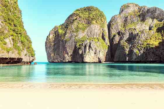 En sandstrand med rolig blått vann, omgitt av høye klipper dekket av vegetasjon. (AI-generert tekst)