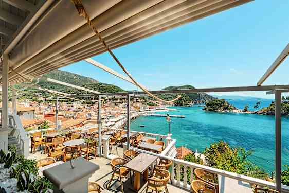 Utsikt fra restaurant mot en bukt med båtplasser, fargerike hus og grønne åser. (AI-generert tekst)