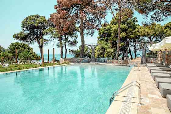 Utendørsbasseng omgitt av solsenger, grøntområder og havutsikt. (AI-generert tekst)