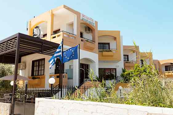 En bygning med gul og hvit fasade samt flagg avbildende Hellas og EU. (AI-generert tekst)