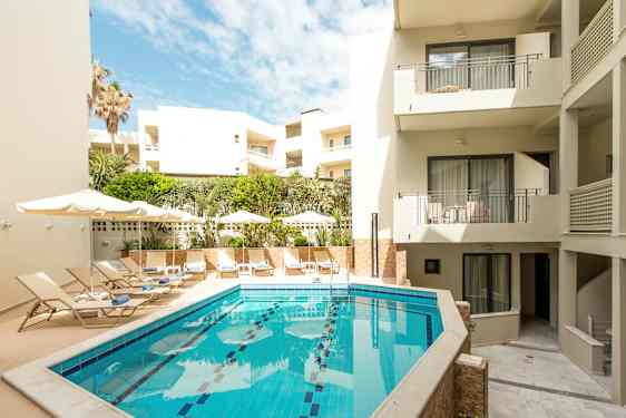 Utendørsbasseng omgitt av solsenger og bygninger. (AI-generert tekst)