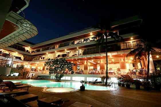 Kveldsvy av en fleretasjes bygning med opplyst fasade og et basseng i forgrunnen. (AI-generert tekst)