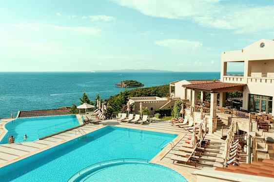 Utsikt over et bassengområde med solsenger og havet i bakgrunnen. (AI-generert tekst)