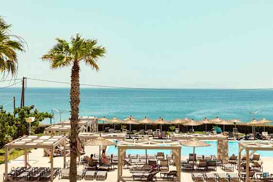 En utsikt over utendørs bassengområde med solsenger, parasoller og havet i bakgrunnen. (AI-generert tekst)