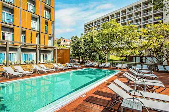 Et basseng med solsenger og bygninger i bakgrunnen. (AI-generert tekst)