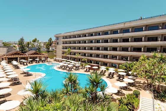 En hotellbygning med balkonger og et basseng omgitt av solsenger og parasoller. (AI-generert tekst)