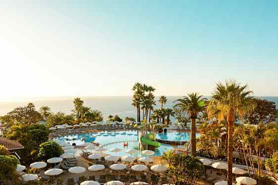 Et utendørsbasseng med solsenger omgitt av palmer og utsikt over havet. (AI-generert tekst)