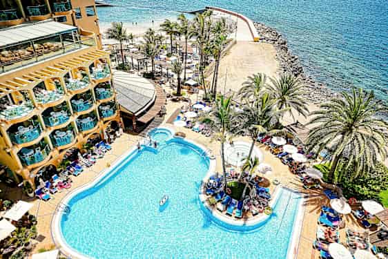 Et hotellbasseng ved kysten med palmer og solsenger rundt. (AI-generert tekst)