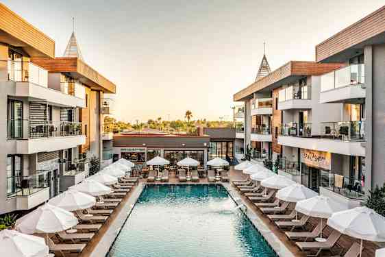 Hotellområde med basseng og solsenger omgitt av bygninger. (AI-generert tekst)