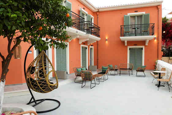 En uteplass med stoler og bord foran en bygning med oransje fasade og grønne skodder. (AI-generert tekst)