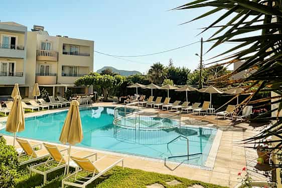 Utendørsbasseng med solsenger og parasoller, omgitt av grøntområder og et hotell i bakgrunnen. (AI-generert tekst)