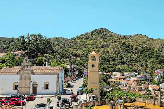 Bilde av en landsby med et klokketårn i forgrunnen, omgitt av hus og grønne åser. (AI-generert tekst)