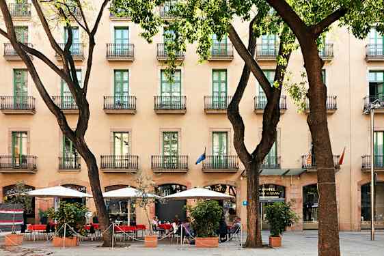 Et hotell med flere etasjer og balkonger, en fortau med parasoller og sitteplasser blant trær. (AI-generert tekst)