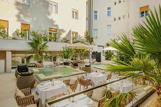 En koselig gårdsplass med bord og stoler i en elegant atmosfære. Det er også grønne planter og et lite basseng. (AI-generert tekst)