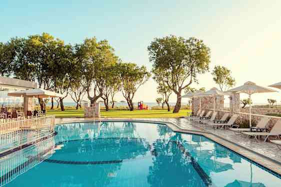 Et basseng med solsenger og parasoller omgitt av grøntområder og trær. (AI-generert tekst)