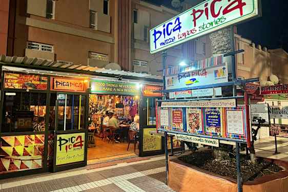 En restaurant med navnet Pica Pica vises om natten. Skilt og menyer pryder eksteriøret. (AI-generert tekst)