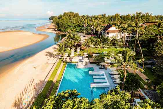Hotellområde ved en strand med basseng og vegetasjon. En elv renner ut i havet. (AI-generert tekst)