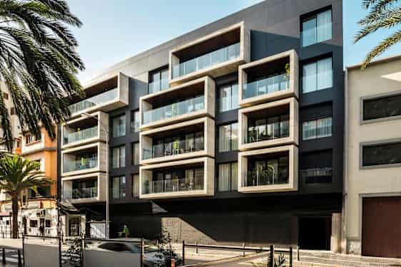Moderne leilighetsbygning med store rektangulære balkonger og glassdetaljer, omgitt av palmer og bymiljø. (AI-generert tekst)