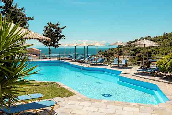 Utendørs basseng med solsenger og parasoller ved siden. I bakgrunnen sees havet og frodig landskap. (AI-generert tekst)