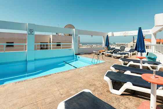 En takterrasse med et basseng og solsenger under en klar blå himmel. (AI-generert tekst)