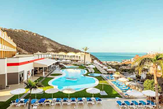 Et feriehotell med et basseng, solsenger og parasoller, omgitt av et fjellandskap og utsikt over havet. (AI-generert tekst)