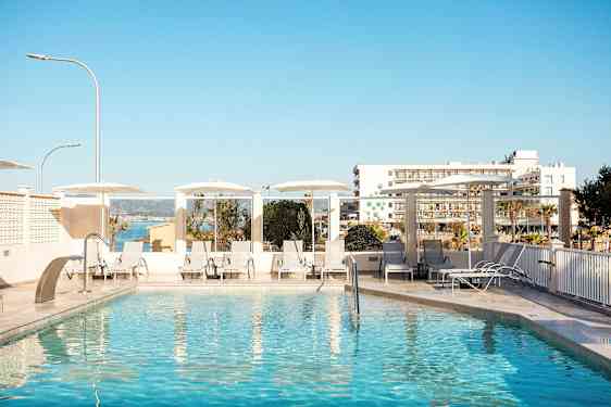 Utendørs basseng med solsenger og parasoller, i bakgrunnen ses bygninger og havet. (AI-generert tekst)