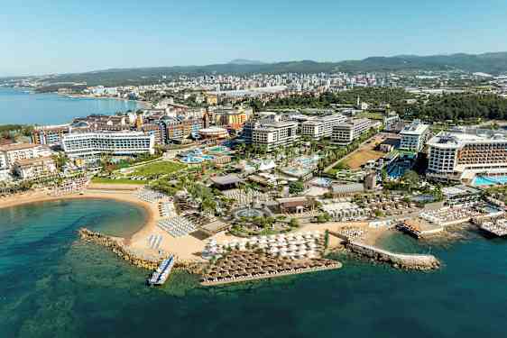 Flyfoto av en ferieby ved kysten med hoteller, bassenger og strand. (AI-generert tekst)