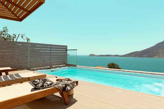 Solstoler ved et basseng med utsikt over havet og fjell. (AI-generert tekst)