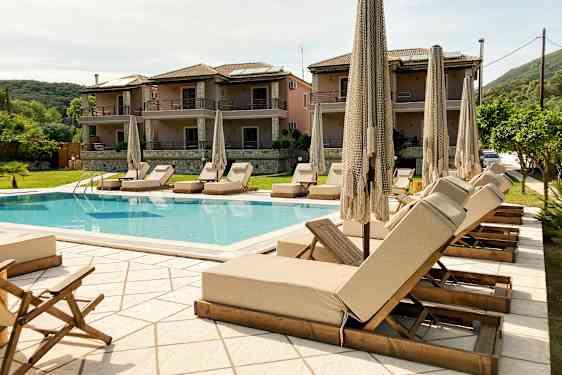 Utendørsbasseng med solsenger og parasoller, omgitt av bygninger og grøntområder. (AI-generert tekst)