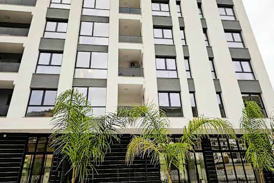 Boligblokk med glassfasade og balkonger, omgitt av palmer. (AI-generert tekst)