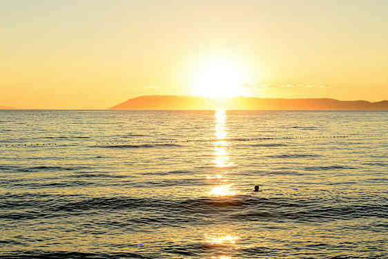 Solnedgang over havet med en silhuett av en svømmende person. (AI-generert tekst)