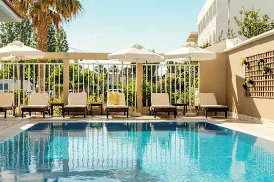 Utendørsbasseng med solsenger og parasoller langs kanten. (AI-generert tekst)