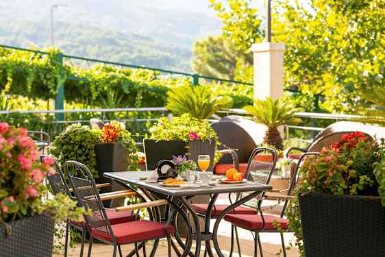 Bord med røde stoler omgitt av grønne planter og fargerike blomster. (AI-generert tekst)