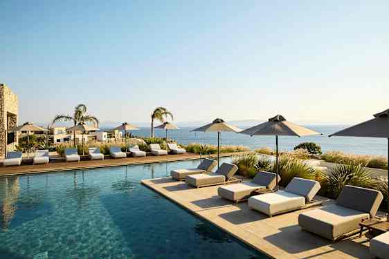 Bassengområde med solsenger og parasoller, utsikt mot havet. (AI-generert tekst)