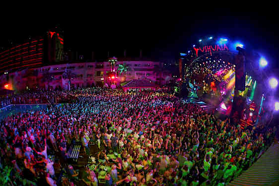 En nattklubb med et publikum foran en fargerikt opplyst scene. (AI-generert tekst)